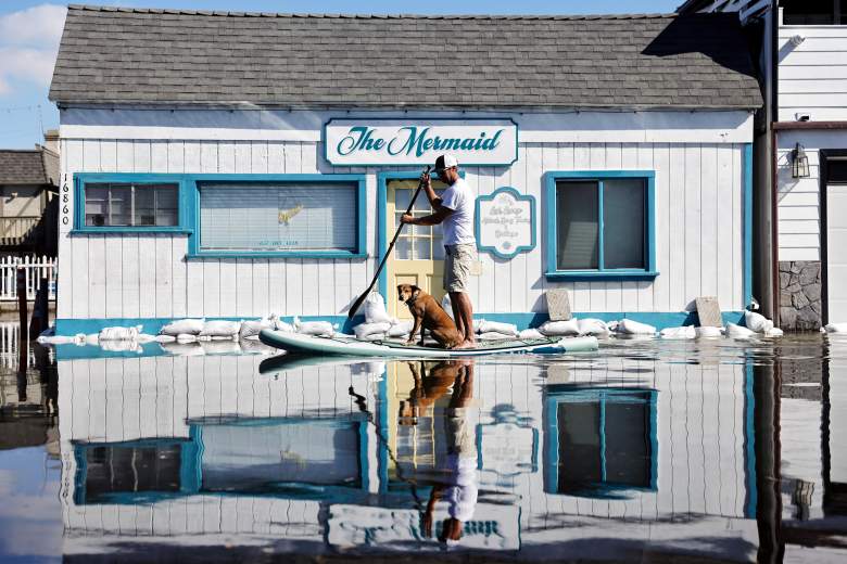 James Hays paddles with his dog Flynn through coastal floodwaters during high tide flooding along Pacific Coast Highway in the Sunset Beach community on October 27, 2026, in Huntington Beach, California.