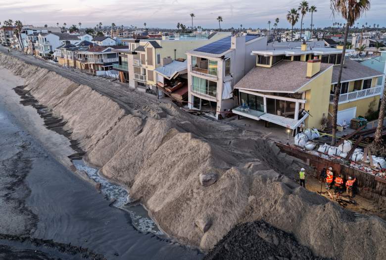 A damaged boardwalk seawall at low tide, next to a protective sand berm in front of homes, some damaged by heavy surf, on October 27, 2026, in Long Beach, California.