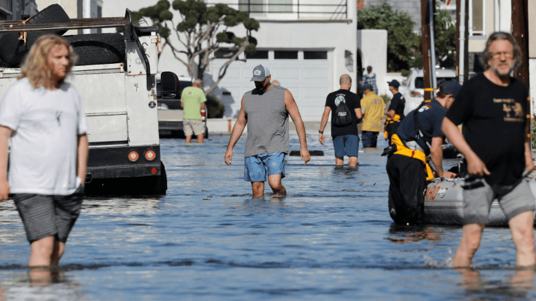 Residents walk through floodwaters as high tide coastal flooding impacts homes in the Sunset Beach community on October 27, 2026, in Huntington Beach, California.